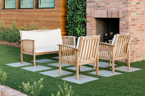 Seating area that includes one bench and two chairs outside on the lawn next to a house